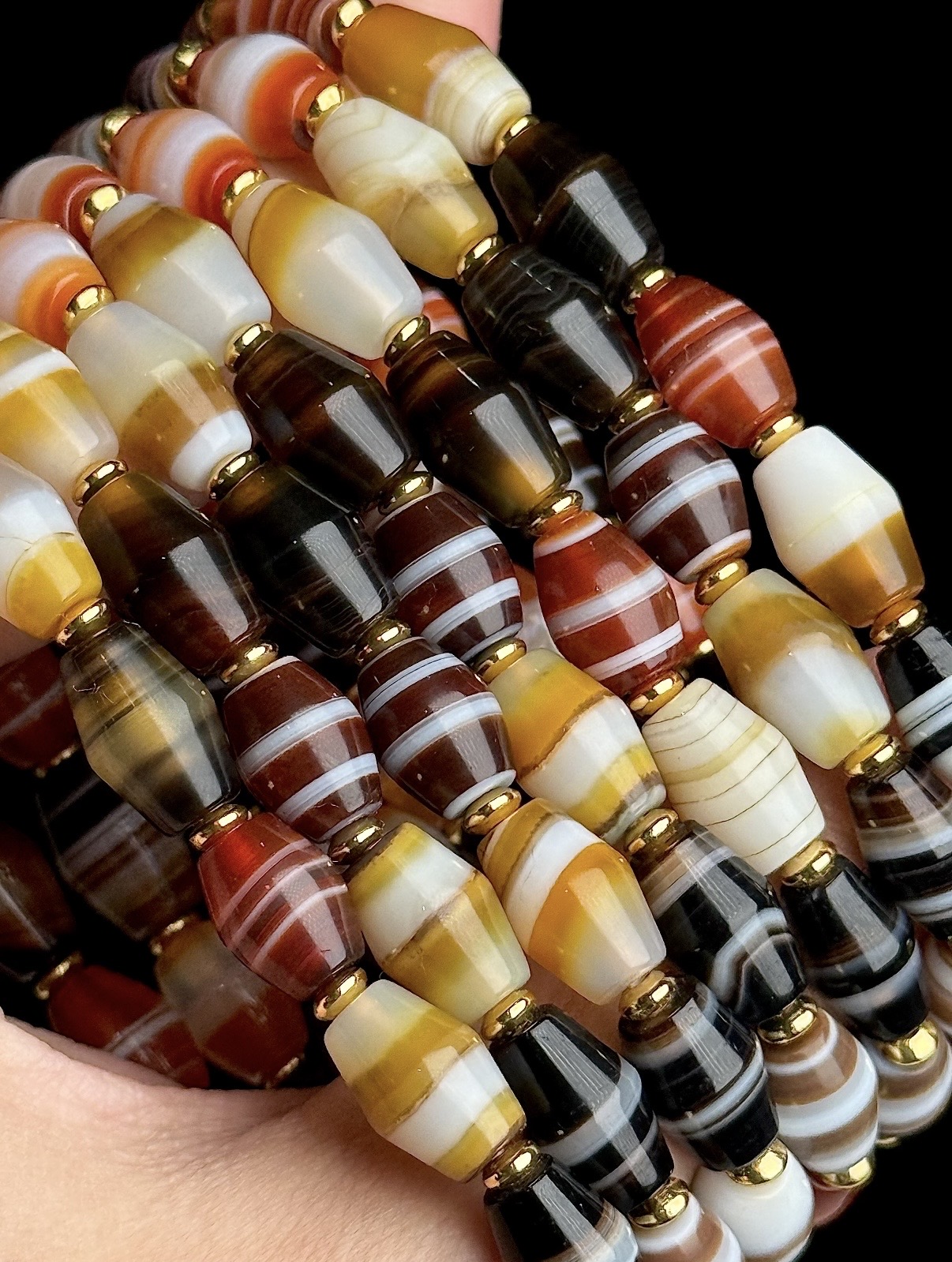 Several strands of banded agate barrel beads in carnelian, honey, bone and smoke, separated by gold spacers.